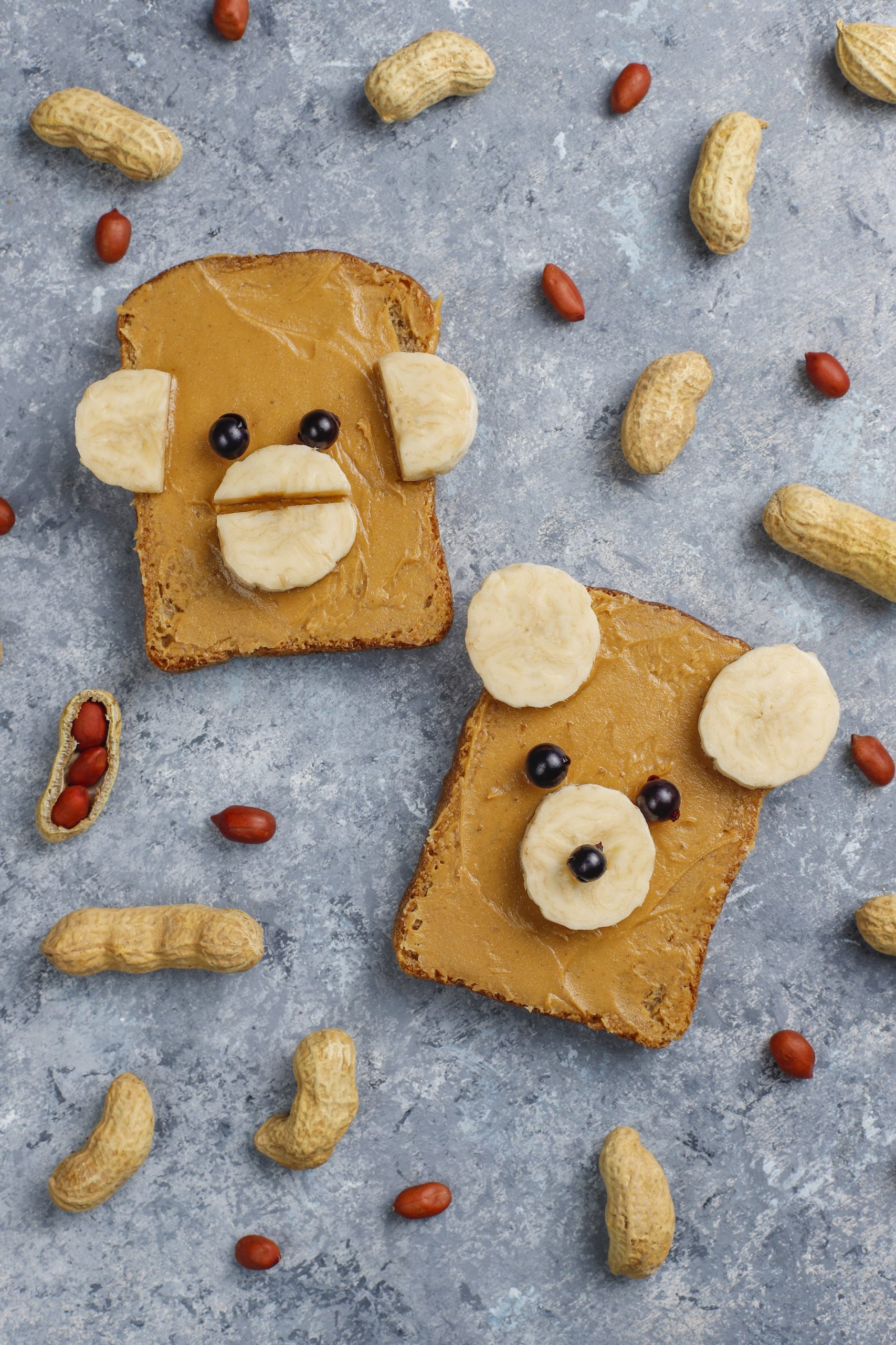 Funny bear and monkey face sandwich with peanut butter, banana and black currant,peanuts on grey concrete background,top view